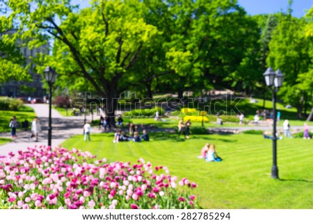 People relax in the city park with flowers in sunny day. Blurry