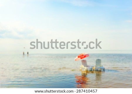 Deck chairs with red umbrella in the sea with an umbrella and a couple playing volleyball. Blurry