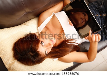 A young woman showing a Tablet PC while laying on the sofa.