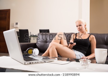 A blonde girl watching TV with the remote control in her hands