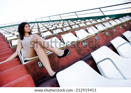 A vintage style dressed girl sitting in a sports stadium alone.