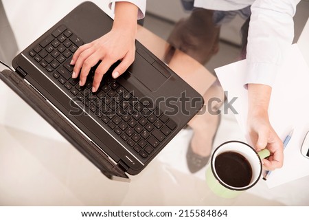 A young blonde secretary holding a cup of coffee seen from above the desk .