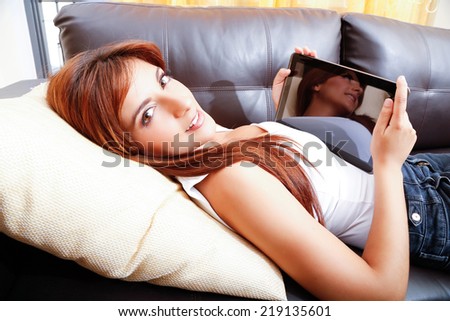 A young woman using a Tablet PC while laying on the sofa.