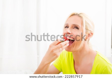 A beautiful mature woman eating strawberry at home.