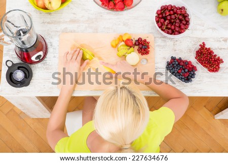 A beautiful mature woman preparing a smoothie or juice with fruits in the kitchen.