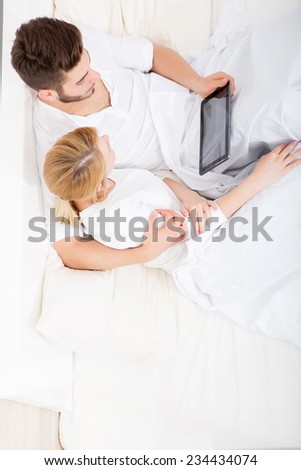 A young and happy couple with a Tablet PC  in Bed.