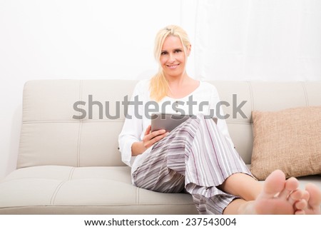 A mature woman in Pyjamas with a Tablet PC on the Sofa.