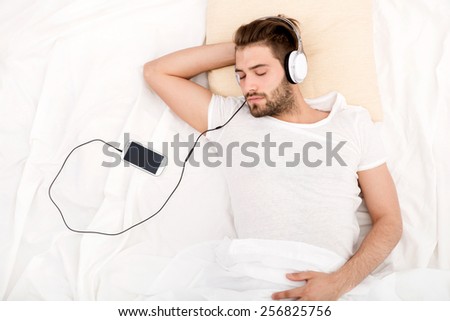 Portrait of a man from above with headphones and smartphone in bed.
