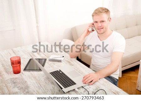 A young caucasian man working in his home office on the phone.