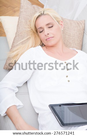 A mature woman in pyjamas relaxing with a tablet PC on the sofa.