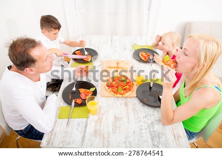 Father and mother with son and daughter eating Pizza for lunch or dinner.