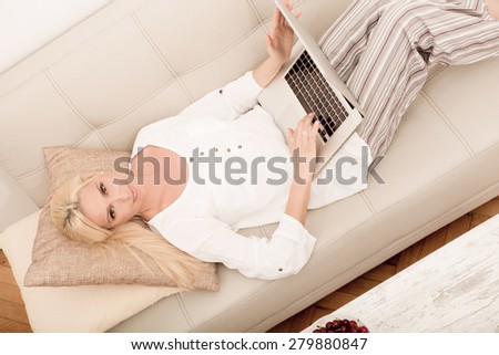 A mature woman with laptop enjoying cherries on the sofa seen from above.