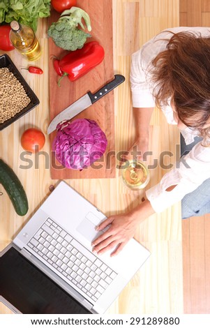 A beautiful mature woman cutting in the kitchen with the help of a computer.