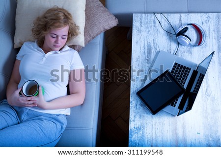 A young plus size woman falling asleep at night on the sofa with a Tablet PC and a Laptop on the Table.