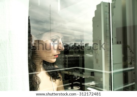 A pensive vintage girl standing behind a window.