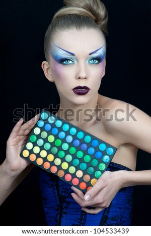 Beautiful woman with a bright makeup holding the box with the shadows to his eyes. Make-up artist