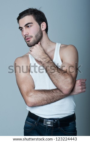 Fashion portrait of the young beautiful man in white t-shirt posing over gray background, series photo