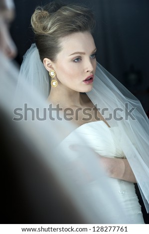 beautiful bride blond girl in white wedding dress with hairstyle and bright makeup looks in the mirror