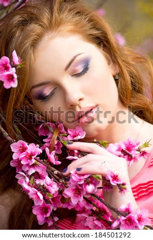 Young pretty woman smelling flowers in blooming peach garden