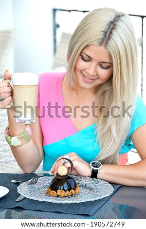 young blonde woman sitting in a cafe in with a cup of coffee latte and chocolate cake