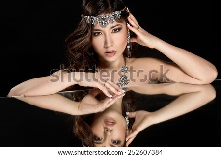 Elegant fashionable woman with jewelry. Beautiful sexy brunette woman with jewelry and her reflection in mirror table on dark with perfect skin