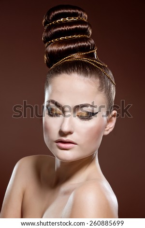 Beauty portrait of attractive model face with bright visage. Gold eye makeup and soft beige lips make-up. Gold arrow make up. Creative hairstyle.