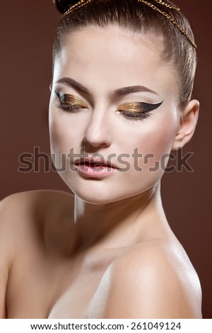 Beauty portrait of attractive model face with bright visage. Gold eye makeup and soft beige lips make-up. Gold arrow make up