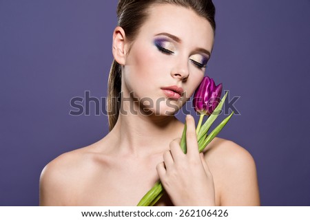Close-up of beautiful woman face with colorful make-up and lips with bight flower. Woman with tulip.