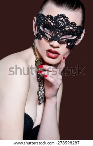 Fashion photo of gorgeous woman with dark hair and blue eyes, with lace mask on her face,posing in dark studio. Sexy Woman.