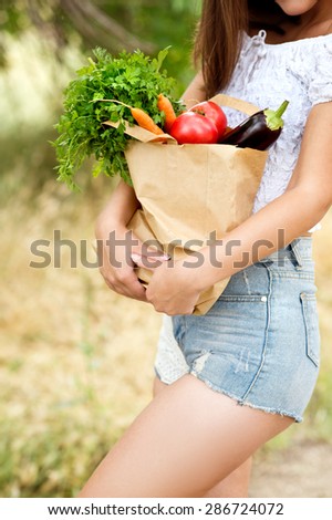 woman holding a vegetable - parsley, pepper, eggplant,carrots, arugula in a paper bag on green background summer nature.