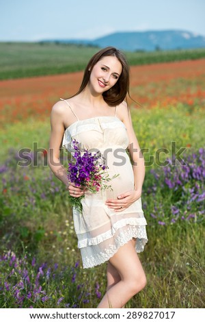 Happy pregnant woman with flower bouquet in meadow flowers, sunset time, new life concept