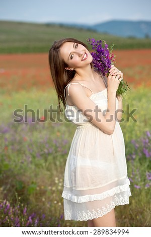 Happy pregnant woman with flower bouquet in meadow flowers, sunset time, new life concept