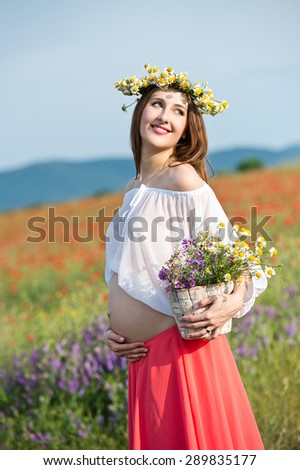 Happy pregnant woman with flower wreath in meadow flowers, sunset time, new life concept
