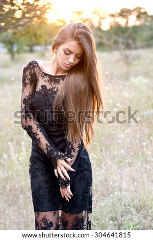 Beautiful sensual woman with dark hair and tanned body,wearing elegant clothes,posing in summer field at sunset