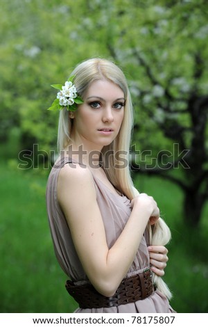 Young beautiful blonde woman in a dress in blooming apple garden with flowers in hair