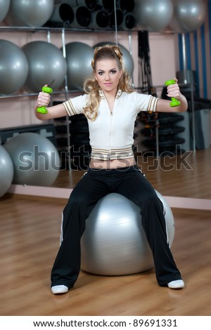 Portrait of fitness woman working out with free weights in gym on fitness ball
