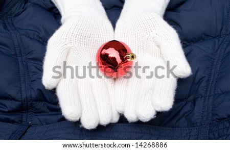 hands in white wool mittens hold red christmas ball