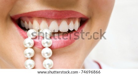 a woman smiles showing white teeth, holding a pearly necklace in to the mouth