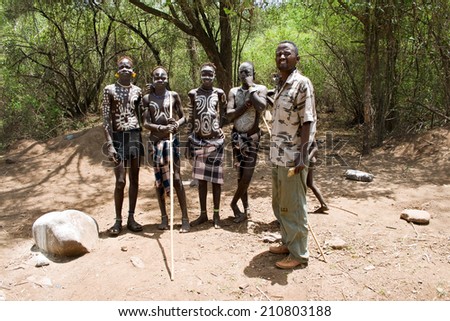 OMO VALLEY, ETHIOPIA - MARCH 13, 2010: Unidentified young adults of the Mursi tribe on the way to their village. Next to them a tourist guide, who is necessary to visit the Omo valley.