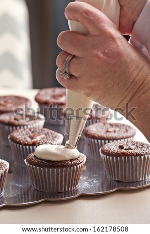 Chef decorating and piping buttercream icing on chocolate filled chocolate cupcakes - hands