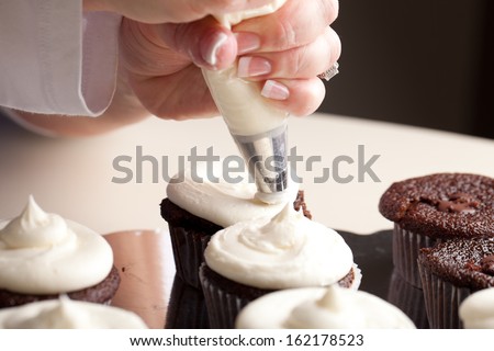 Chef decorating and piping buttercream icing on chocolate filled chocolate cupcakes - bakery