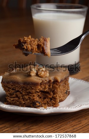 Macro shot of carrot cake topped with a walnut with a bite on a fork next to a glass of cold milk