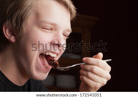 Handsome young Caucasian male eating a bite of decadent chocolate peanut butter cake