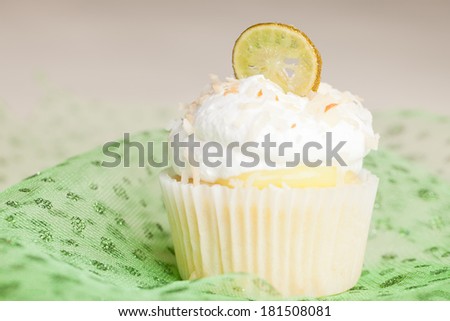 Coconut Key Lime Cupcake on green St. Patrick\'s Day fabric and a white background - Coconut cake with a key lime filling topped with a light frosting, toasted coconut, and a slice of candied key lime