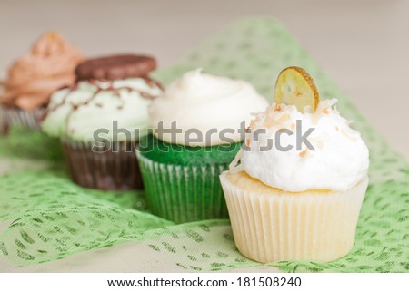 Coconut Key Lime Cupcake, Pot of Gold Chocolate Caramel Cupcake, Irish Mint Chocolate Cupcake, and Green Velvet Cupcake topped with cream cheese frosting on green tule and a white background