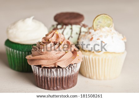 Coconut Key Lime Cupcake, Pot of Gold Chocolate Caramel Cupcake, Irish Mint Chocolate Cupcake, and Green Velvet Cupcake topped with cream cheese frosting on a vintage off white wooden table