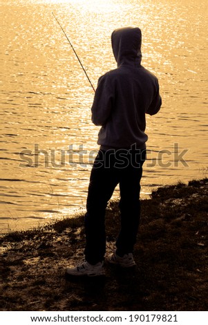 Silhouette of a young teenage man fishing at sunset