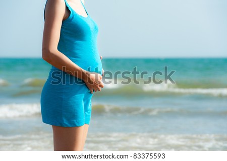 woman in blue shirt is holding pregnant belly