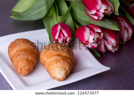 Two croissants on a plate next to a bouquet of tulips