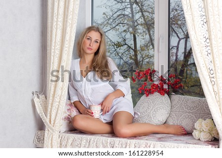 Portrait of charming girl in sweater holding cup and looking through window